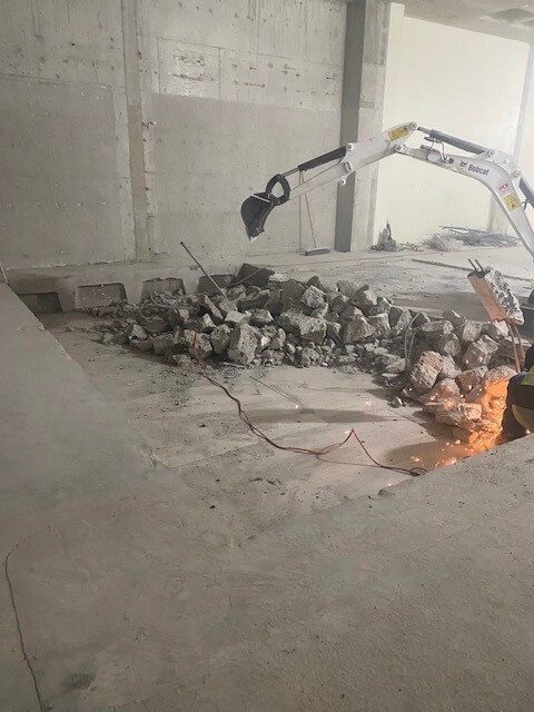 An excavator cuts through concrete floor