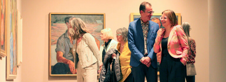 Multiple people look at art at Glenbow's satellite gallery Glenbow at The Edison. Two individuals smile and talk together.